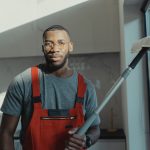 A professional cleaner holding a tool indoors, dressed in red overalls with natural light.
